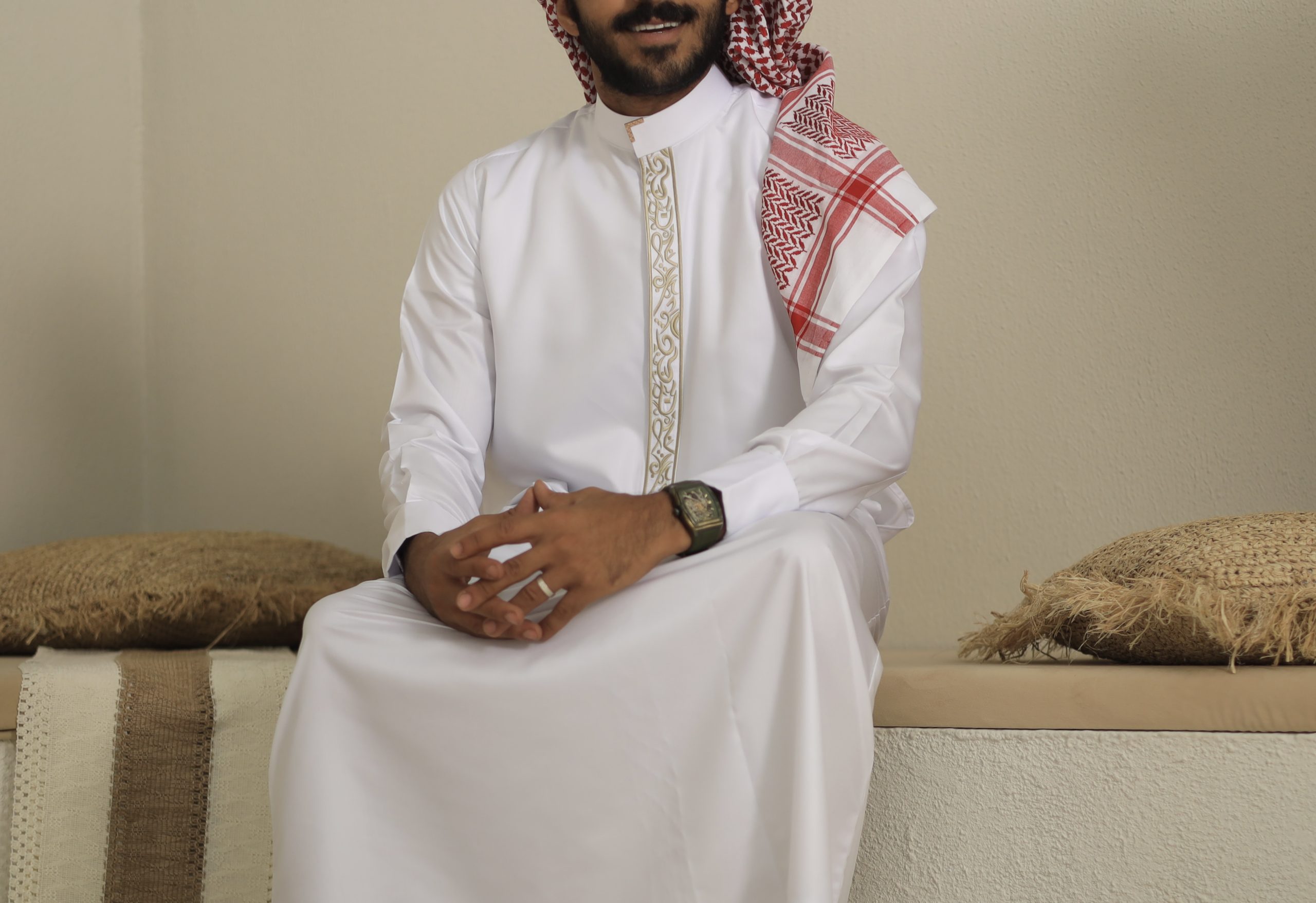 Man wearing the Al Aniq White Collar Thobe with gold embroidery and a red shemagh