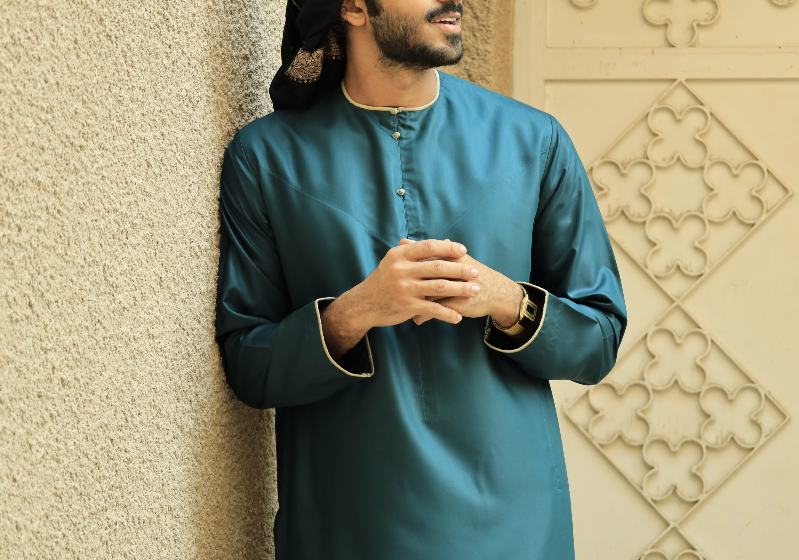 Man wearing a teal green Emirati thobe in front of a patterned wall